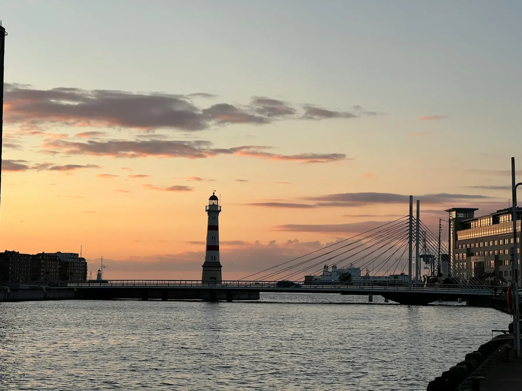 Inre hamnen i Malmö i solnedgång, med en röd och vit fyr och en snedkabelbro över vattnet.